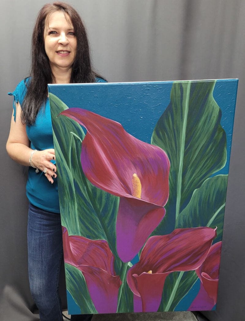 Artist, Nanda Lamprecht, holding her original acrylic painting of calla lilies