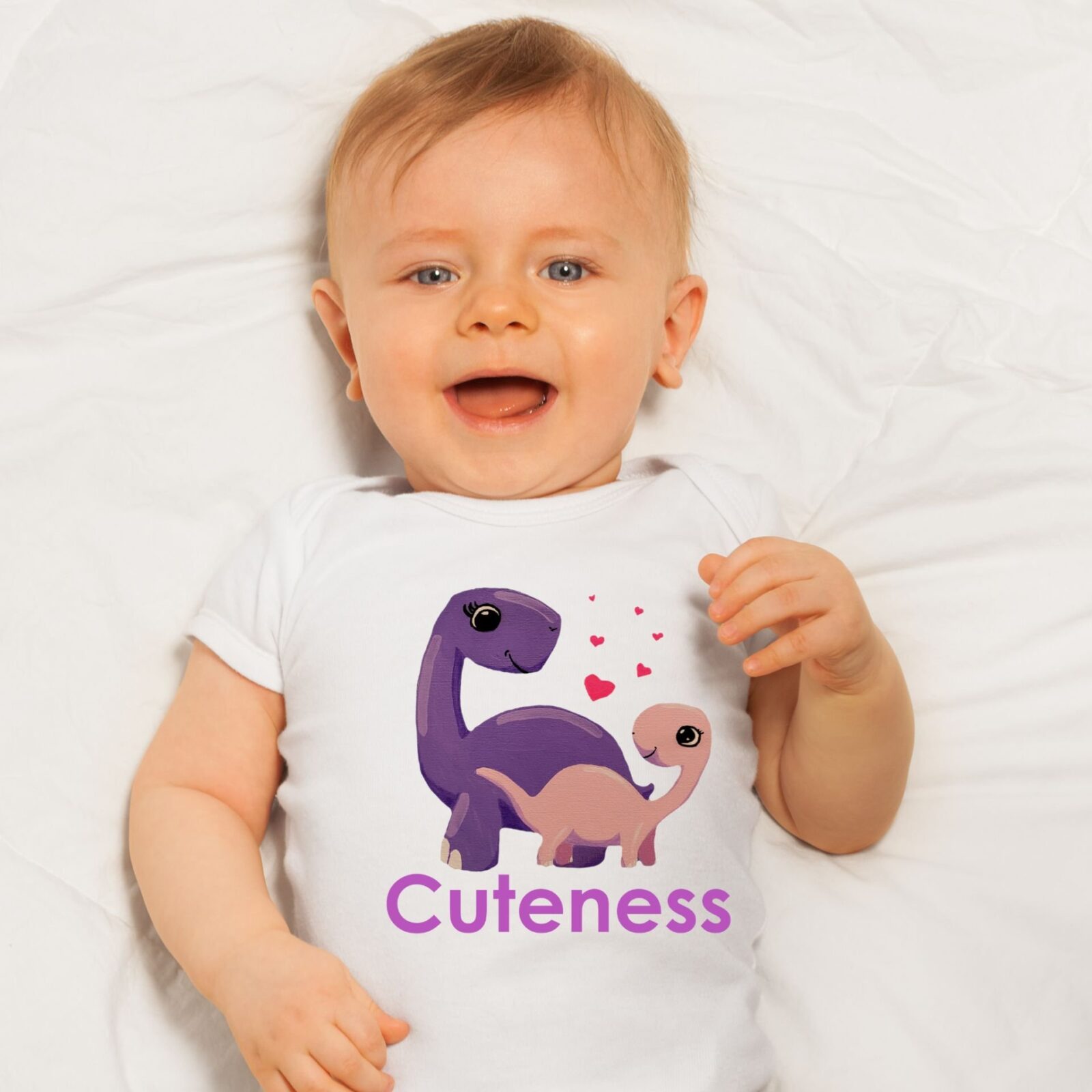 Baby wearing a white summer bodysuit with a dinosaur design, and the word "Cuteness" which is optional to personalize to the name of your baby.