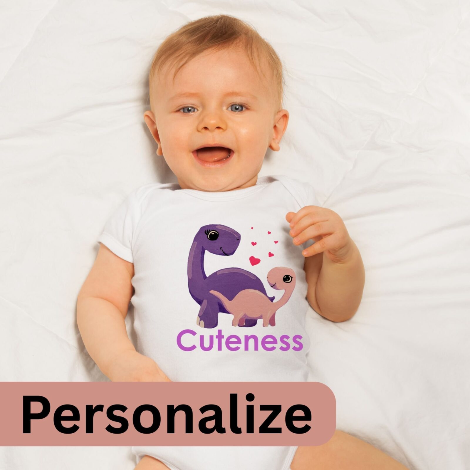 Baby wearing a white summer bodysuit with a dinosaur design, and the word "Cuteness" which is optional to personalize to the name of your baby.