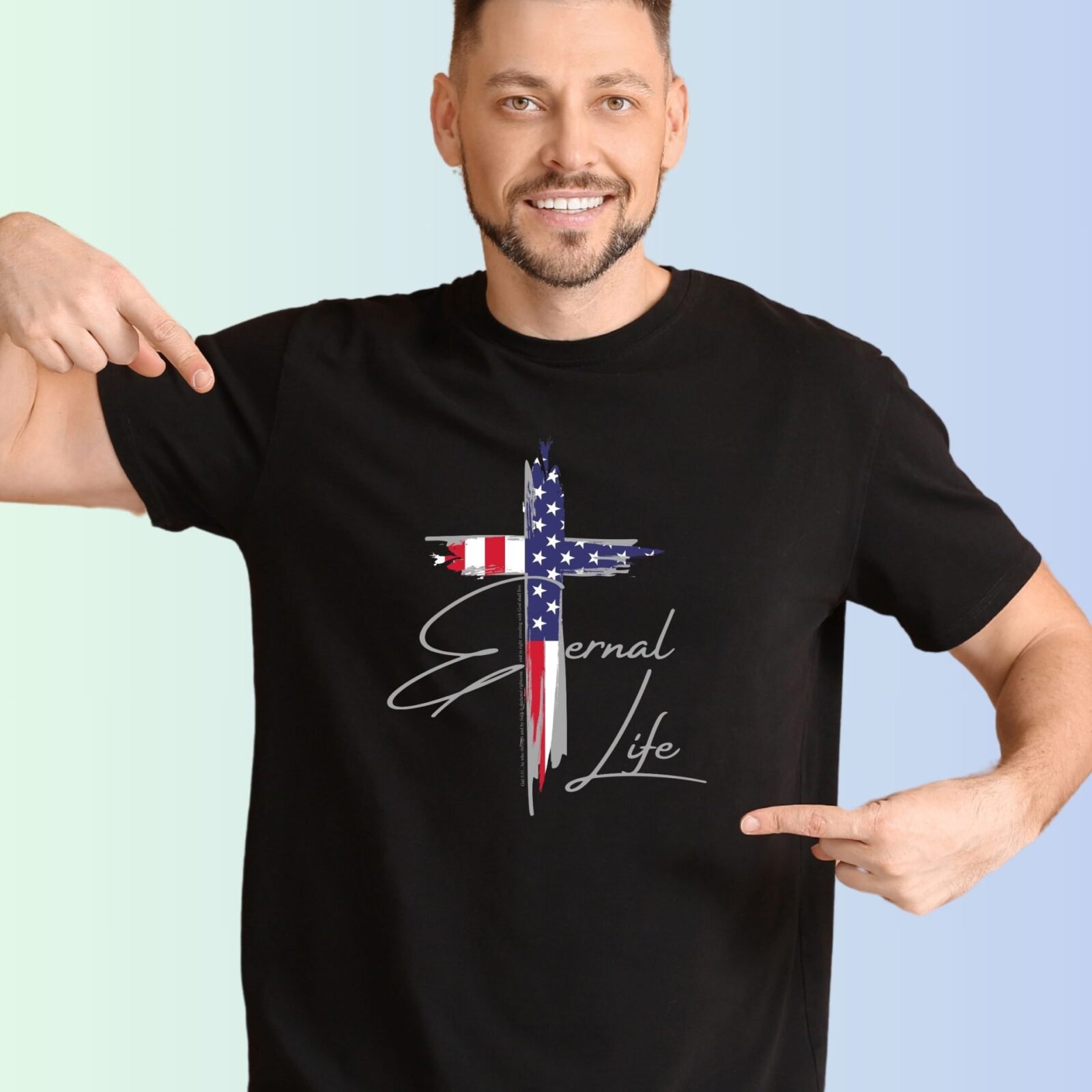 A man wearing a black unixes t-shirt with a cross design. This Christian Cross design with the USA flag includes the text "Eternal Life" and quote Galatians 3:11.
