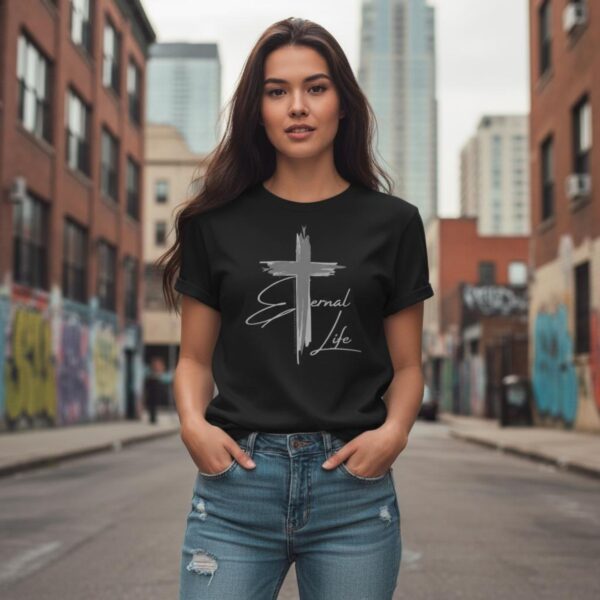 Eternal Life Plain Cross Black Tshirt Woman in City A woman wearing a black unisex t-shirt with a Plain Cross design. This Christian Cross design with the Canadian flag includes the text "Eternal Life" and quote Galatians 3:11.