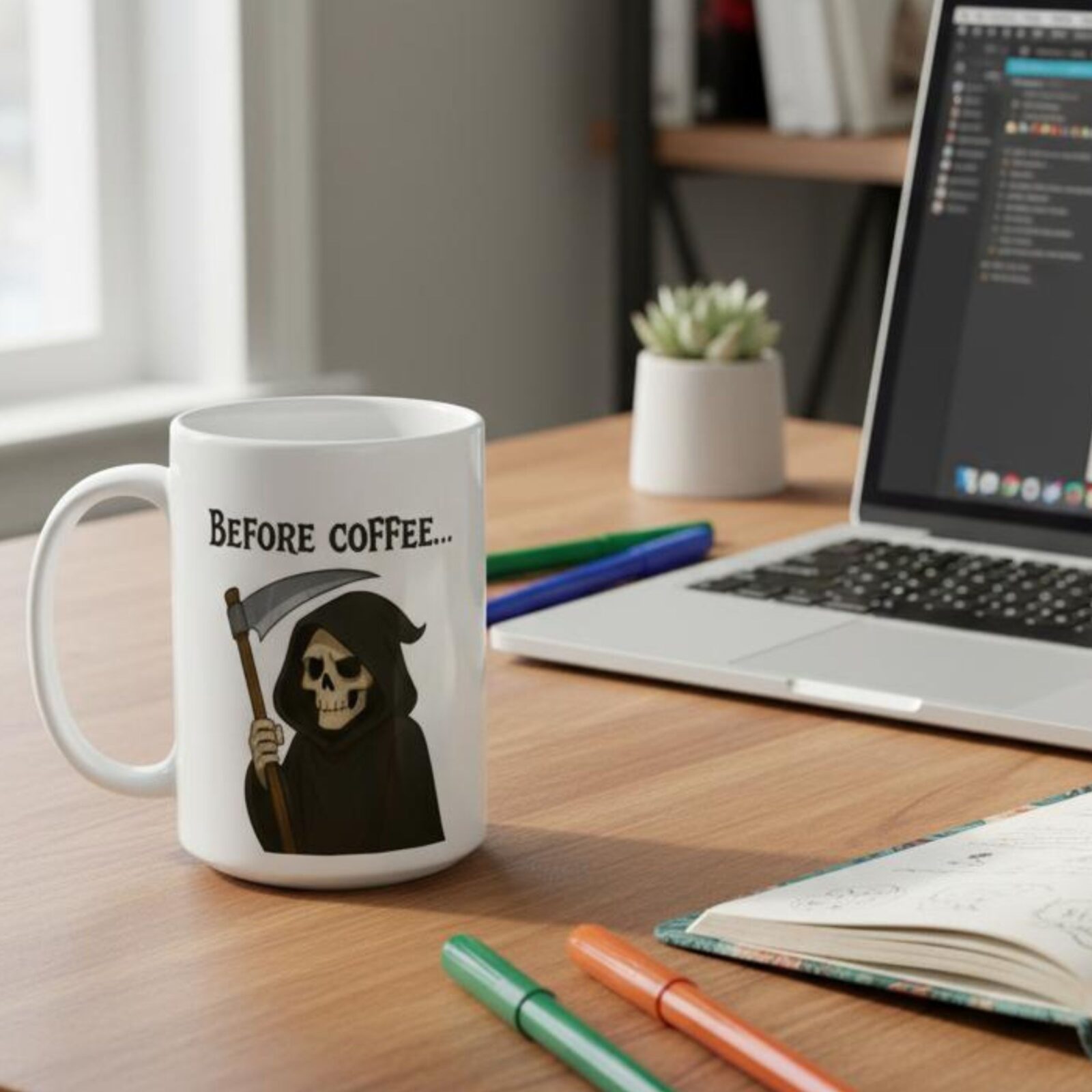 The Grim Reaper coffee mug standing on an office desk next to a laptop.