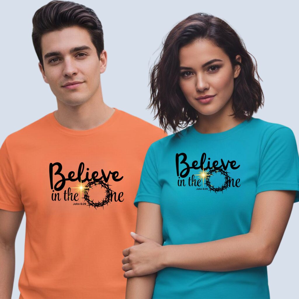 A man wearing a coral unisex t-shirt and a woman wearing an aqua unisex t-shirt, both with a religious design and the text "Believe in the One" relating to John 6:29.