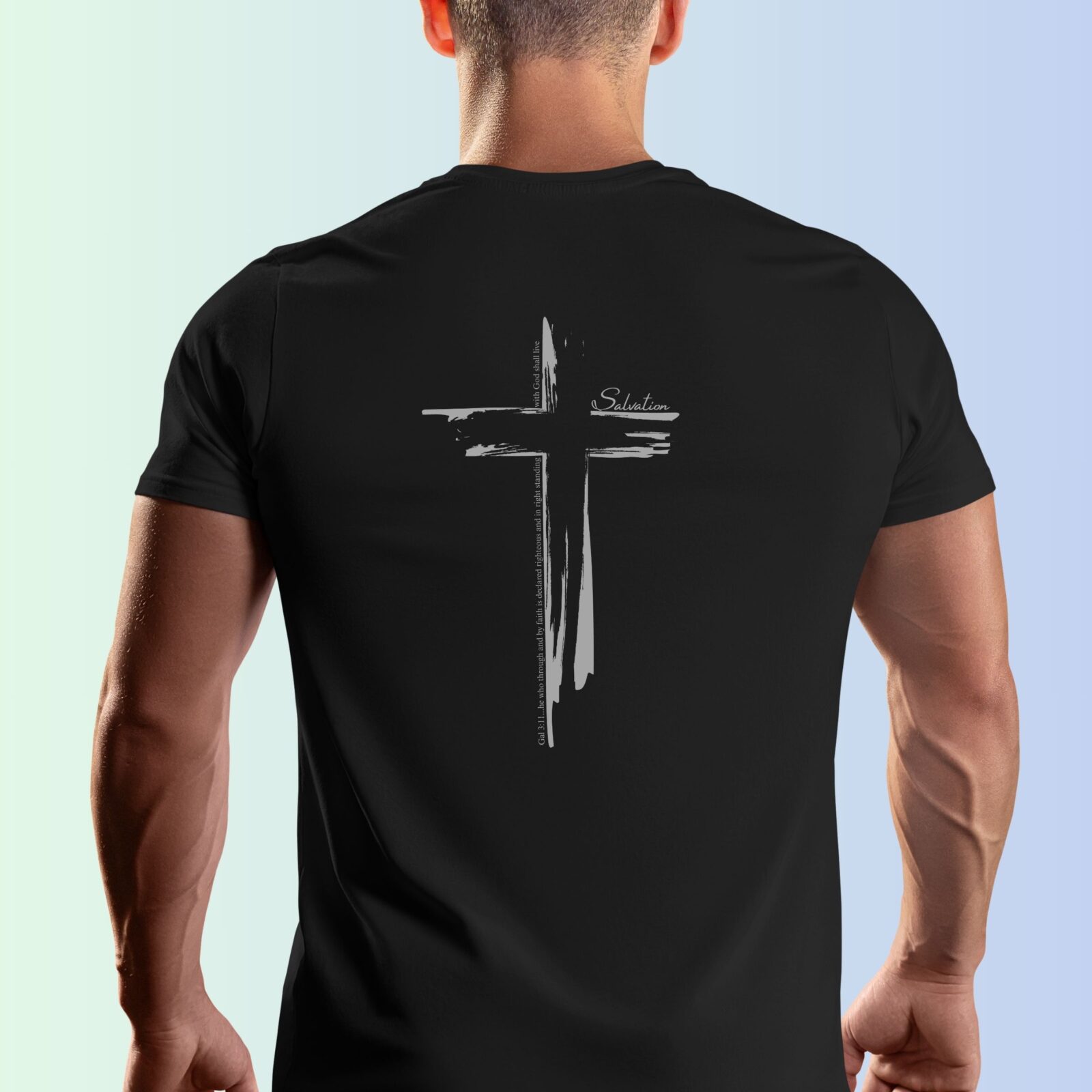 A man wearing a black t-shirt with a cross design on the back of the shirt. This Christian Cross design includes the text "Salvation" and quote Galatians 3:11.