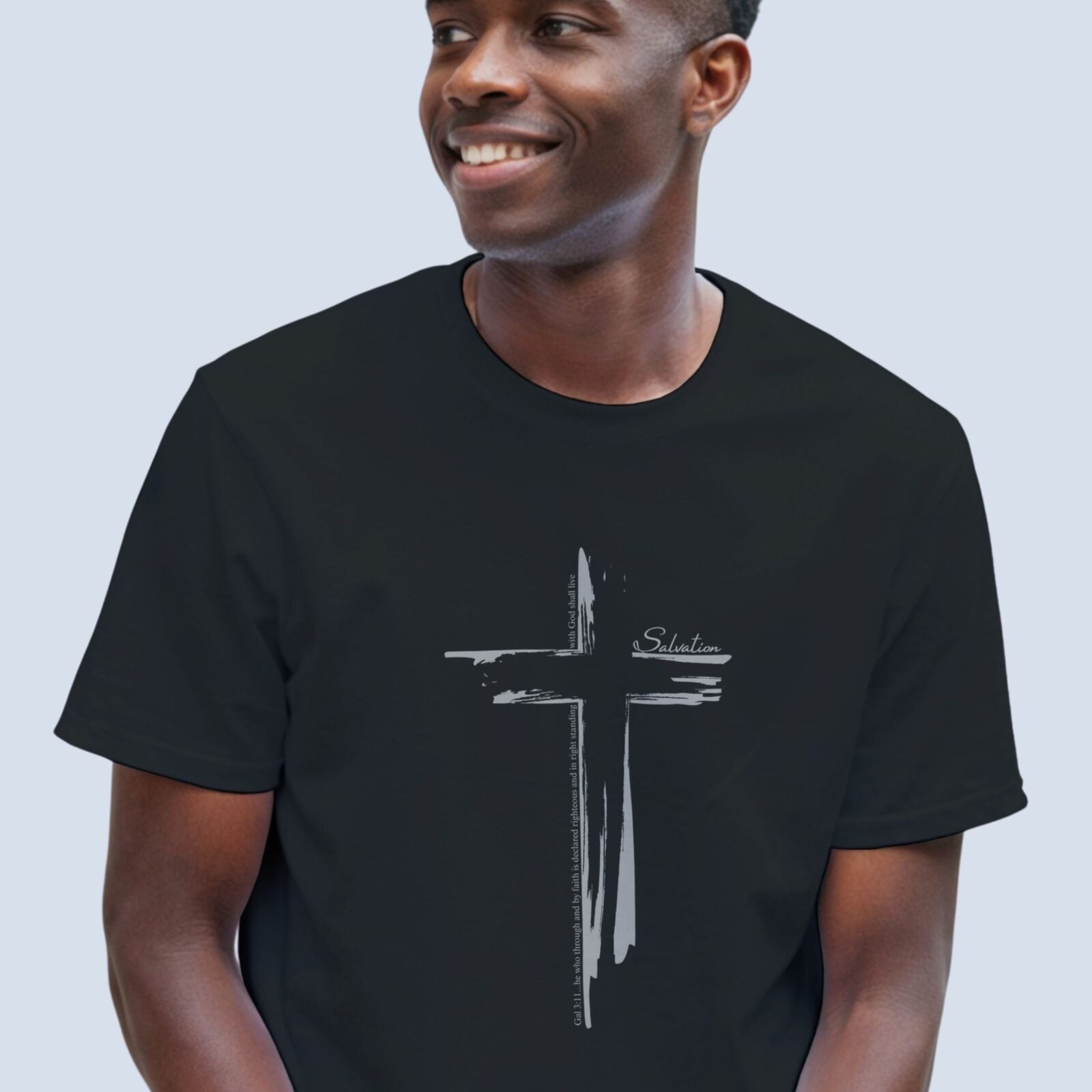 A man wearing a black t-shirt with a cross design on the front of the shirt. This Christian Cross design includes the text "Salvation" and quote Galatians 3:11.