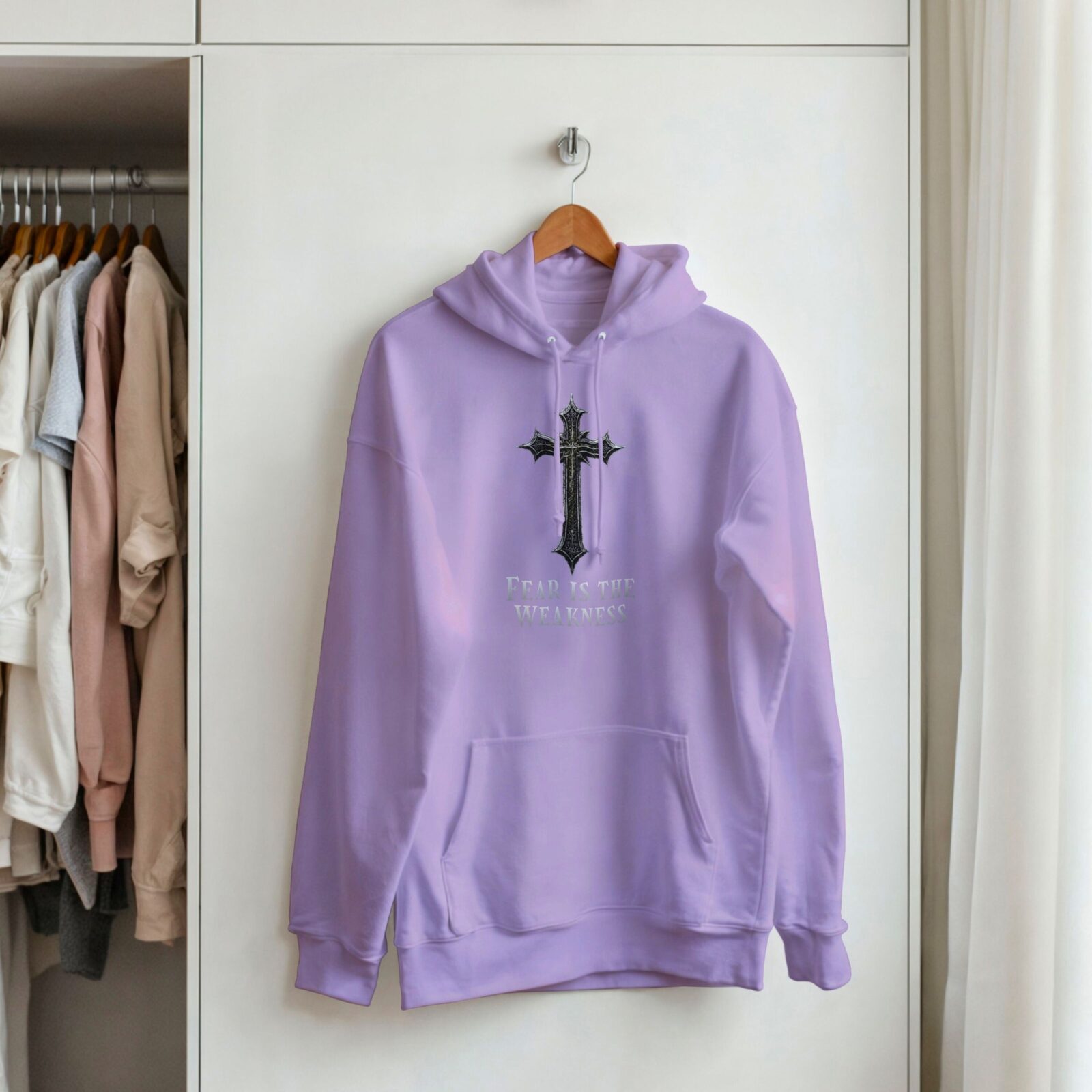 Fear is the Weakness Orchid purple pullover hoodie with a cross design hanging on a cupboard door