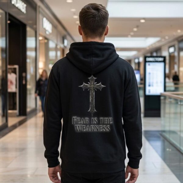 Fear is the Weakness Zip Hoodie Man Black A man wearing a black unisex zipper hoodie with a cross design and the text "Fear is the Weakness" printed on the back of the hoodie.