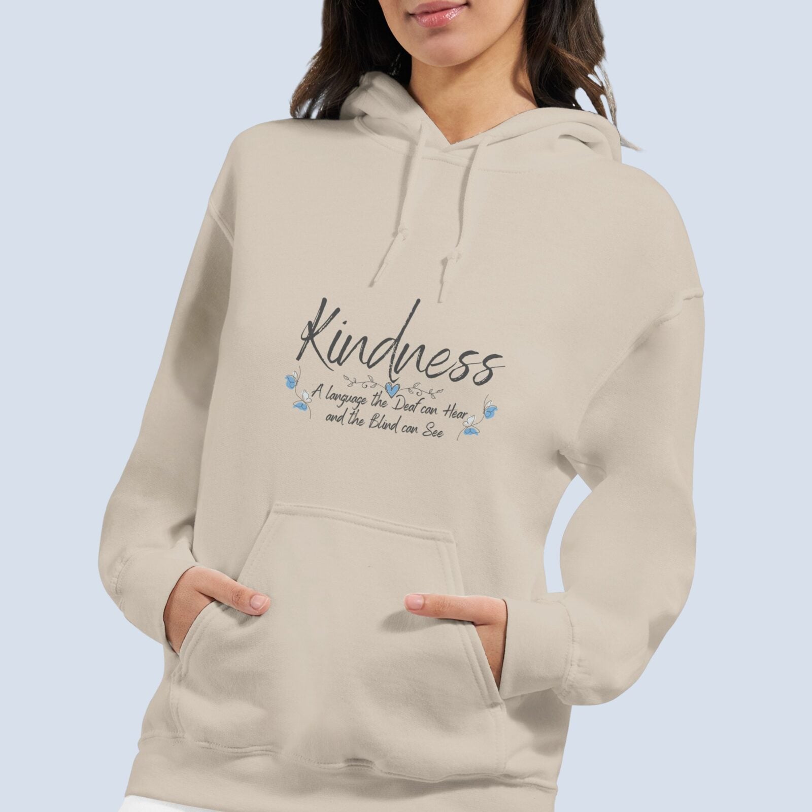 A woman wearing a sand coloured pullover hoodie with a butterfly design and the text "Kindness, a language the deaf can hear and the blind can see".