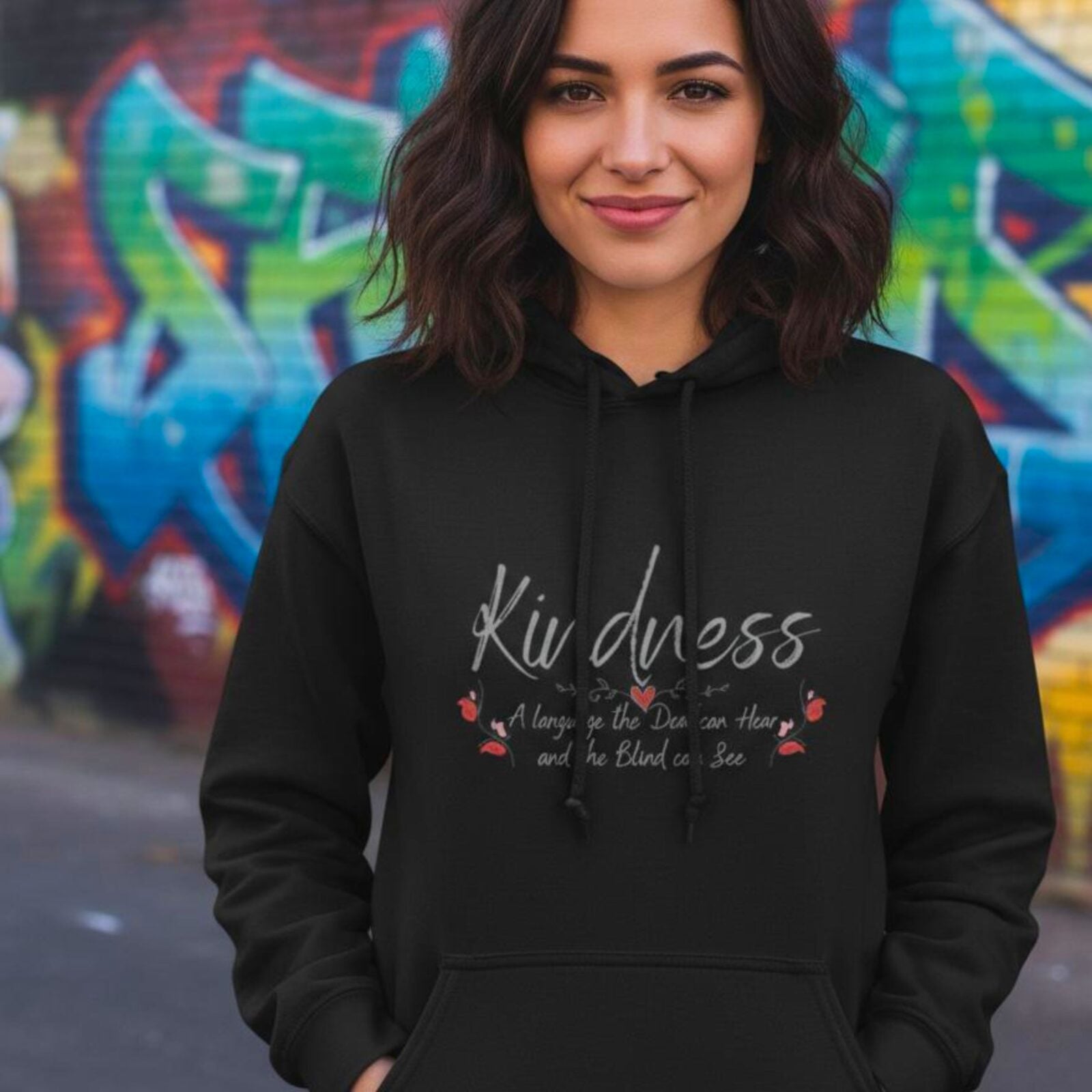 A woman wearing a black pullover hoodie with a butterfly design and the text "Kindness, a language the deaf can hear and the blind can see".