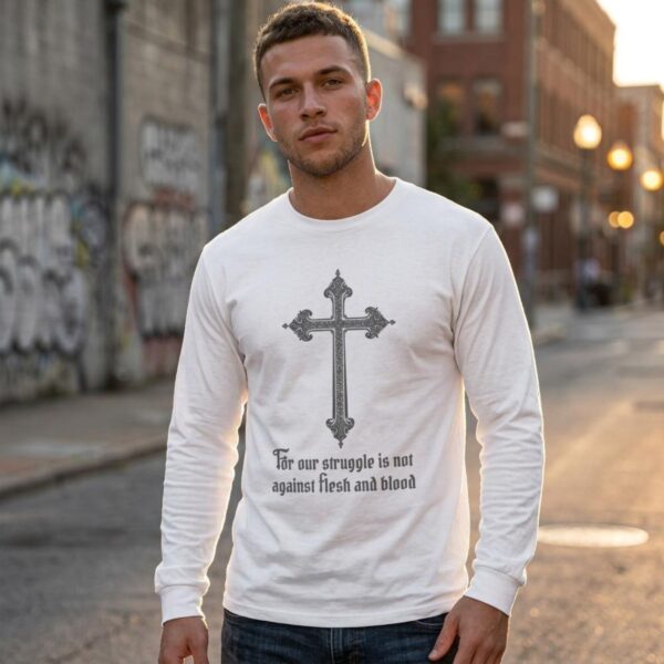 A man wearing a white unisex long sleeve t-shirt with the cross design and the text "For our struggle is not against flesh and blood"
