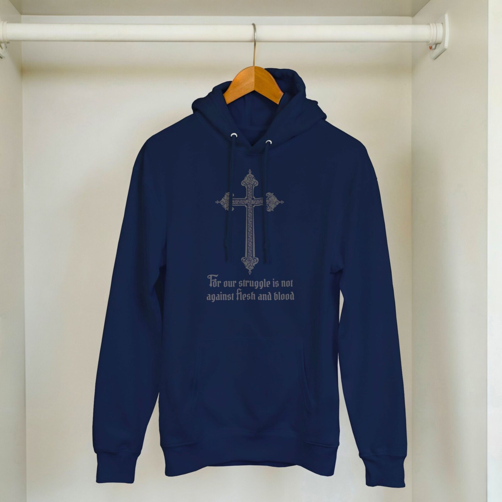 A navy unisex pullover hoodie with a cross design and the text "For our struggle is not against flesh and blood", hanging in a cupboard.