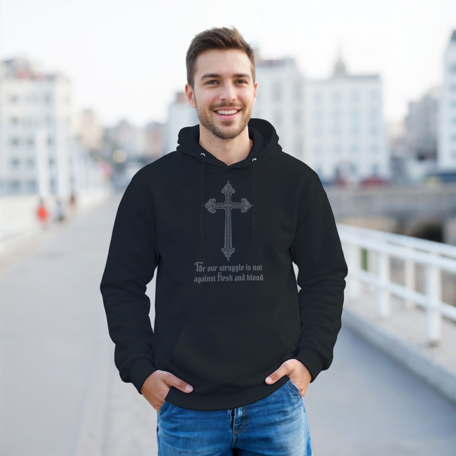 A man wearing a black unisex pullover hoodie with a cross design and the text "For our struggle is not against flesh and blood".