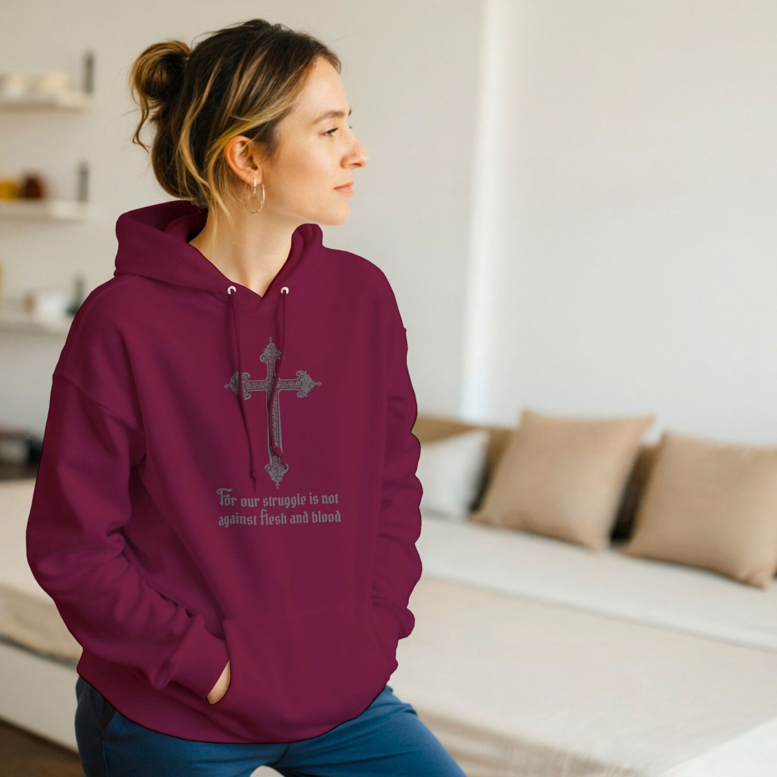 A woman wearing a maroon unisex pullover hoodie with a cross design and the text "For our struggle is not against flesh and blood".
