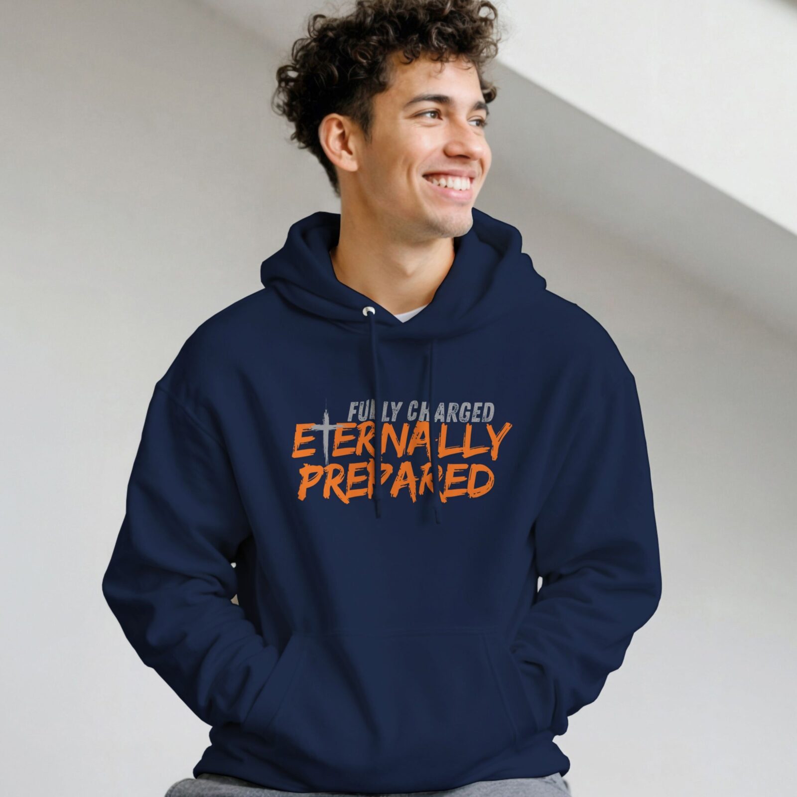 A man wearing a navy unisex pullover hoodie with a cross and the text "Fully Charged, Eternally Prepared".
