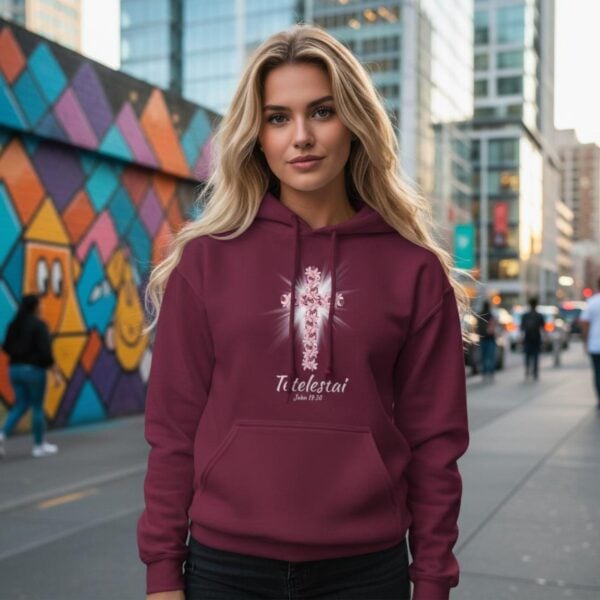 A woman wearing a maroon pullover hoodie with a lily cross design and the text "Tetelestai, John 19:30".