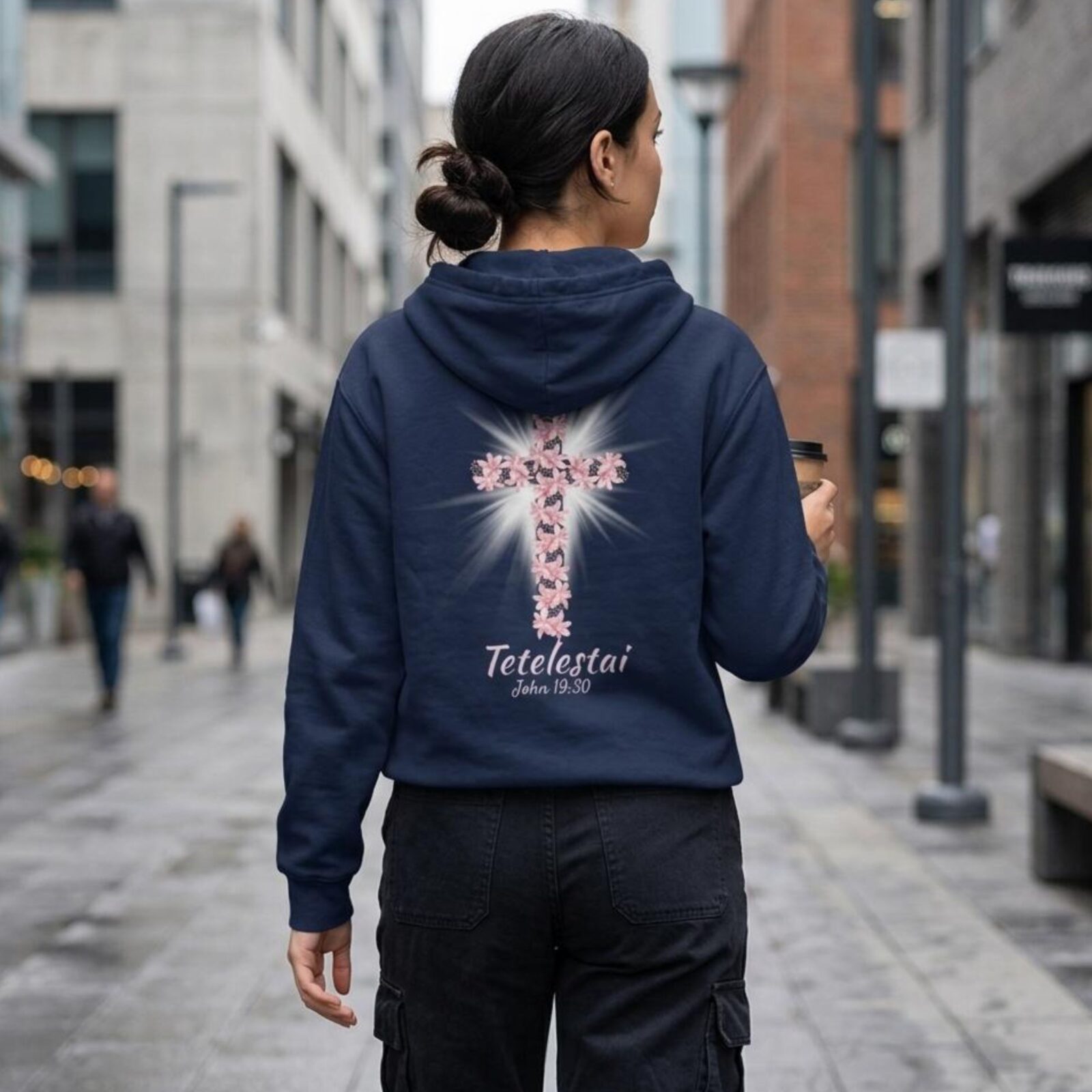 A woman wearing a navy zipper hoodie featuring a lily cross design with the text "Tetelestai, John 19:30" printed on the back of the zip hoodie.