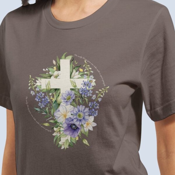 A woman wearing a pebble brown Christian t-shirt with the design of a boho style cross covered with purple flowers and the text: "The only thing you can take with is your people".