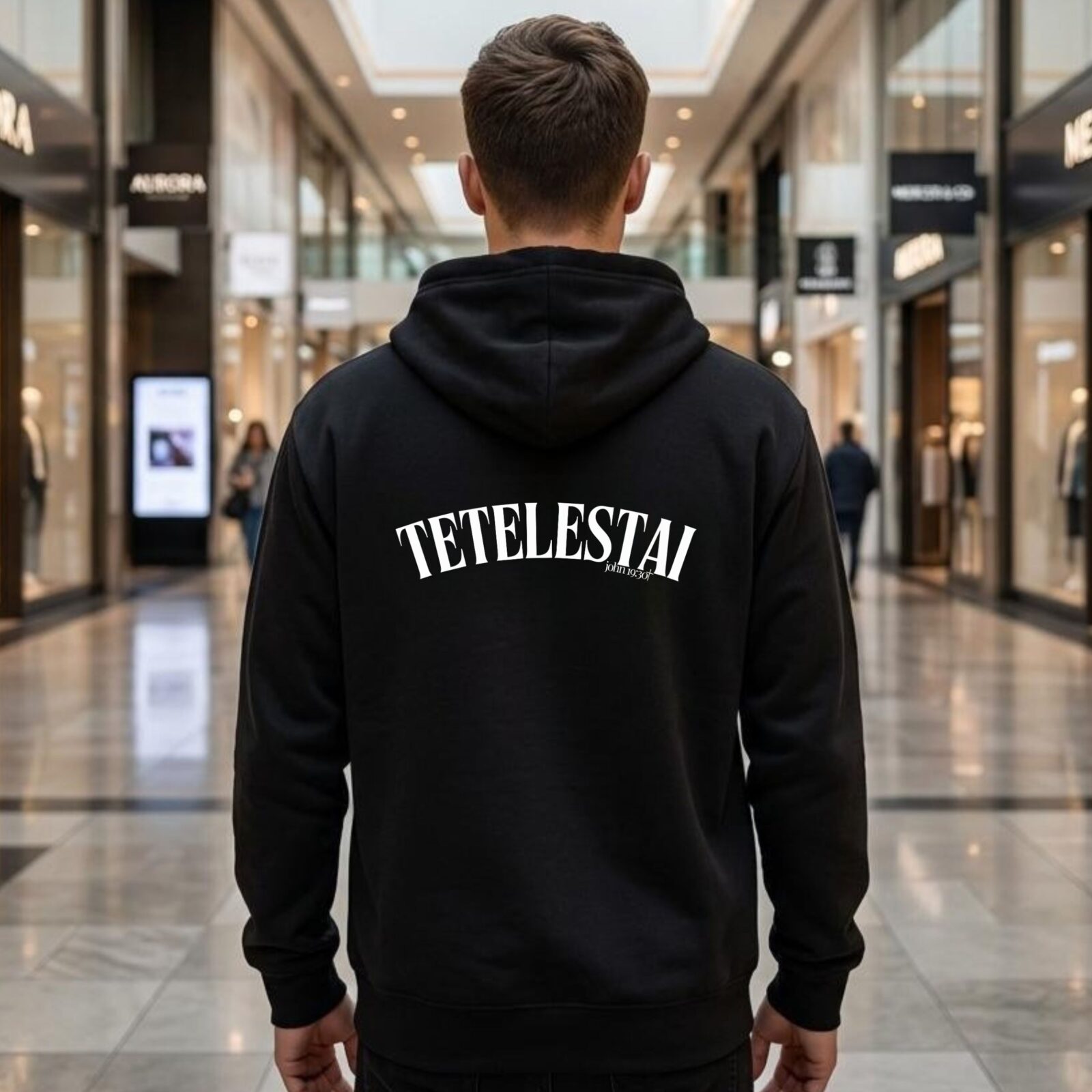 A man wearing a navy unisex zipper hoodie with the text "Tetelestai" and "John 19:30" printed on the back.
