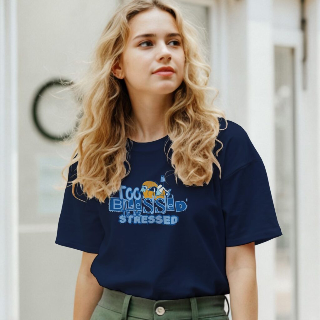 A woman wearing a navy unisex Christian t-shirt featuring the declaration “Too Blessed To Be Stressed” and a graphic of a woman relaxing with her cat, printed on the front of the t-shirt.