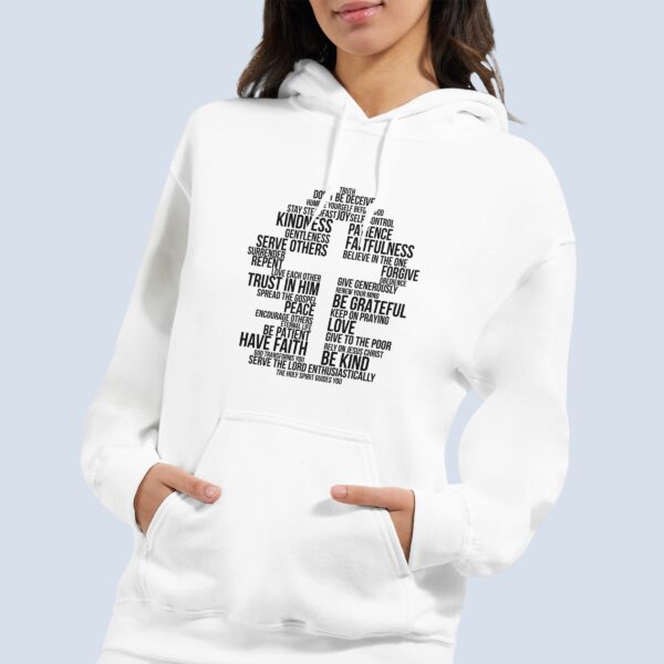 A woman wearing a white unisex pullover hoodie with a cross surrounded by uplifting Christian phrases including Be Kind, Surrender, Trust in Him, and Give to the Poor, printed on the front.