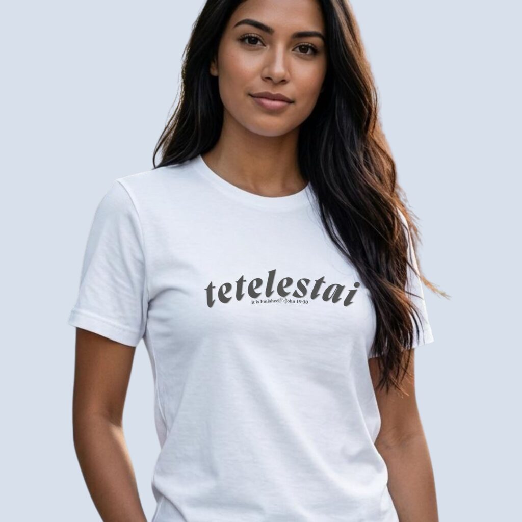 A woman wearing a white unisex Christian t-shirt featuring the powerful words “Tetelestai” and “John 19:30” alongside a delicate heart and cross graphic, printed on the front of the t-shirt.