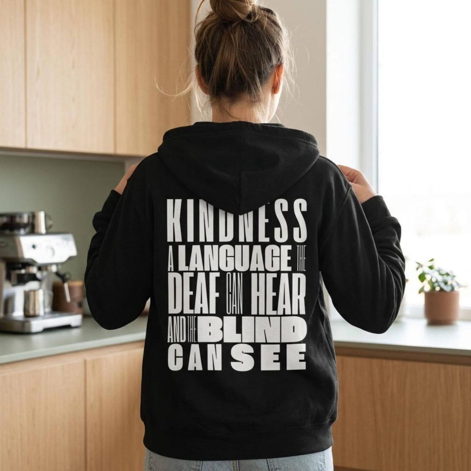 A woman wearing a black unisex full zip up hoodie with an inspirational message "Kindness, a language the deaf can hear and the blind can see". The design on this Christian hoodie is printed on the back of the hoodie only.