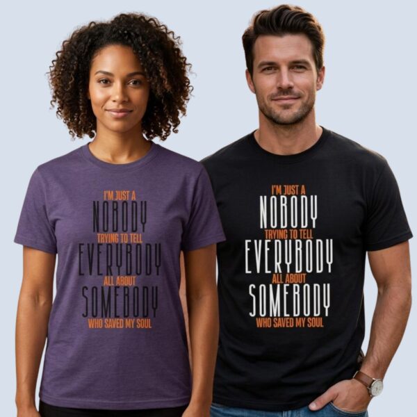 A woman wearing a heather purple coloured unisex Christian t-shirt and a man wearing a black coloured unisex Christian t-shirt, both with the inspirational religious text "I’m just a nobody trying to tell Everybody all about Somebody Who saved my soul". The message celebrates the One who saves and encourages us to tell others about Jesus.